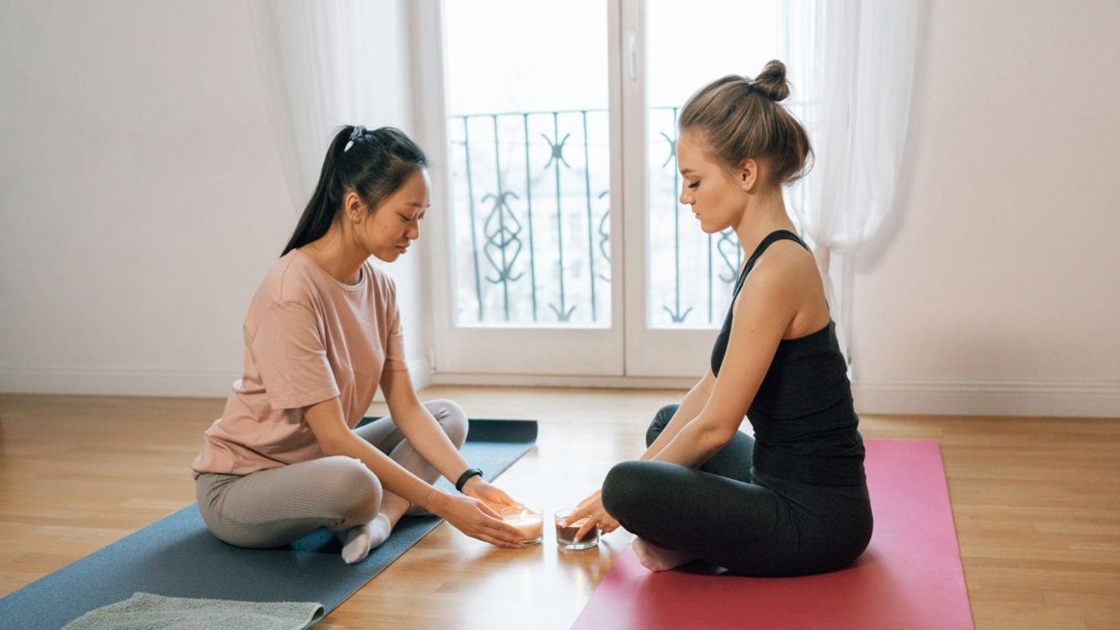 Two women seated facing one another on yoga mats, one with blonde hair in a bun