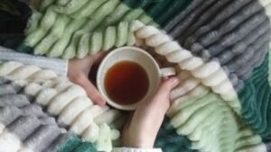 Hands holding a cup of tea against a soft textured blanket