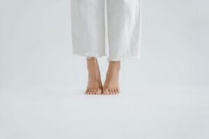 Bare feet in white trousers standing on a plain white floor