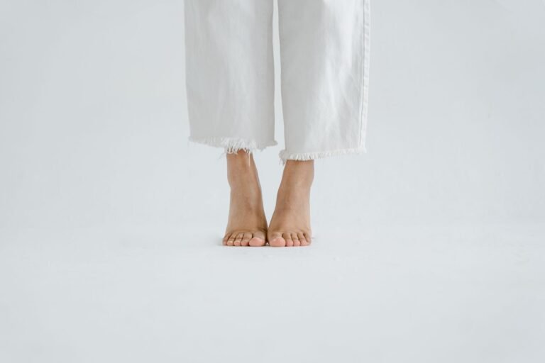 Bare feet in white trousers standing on a plain white floor