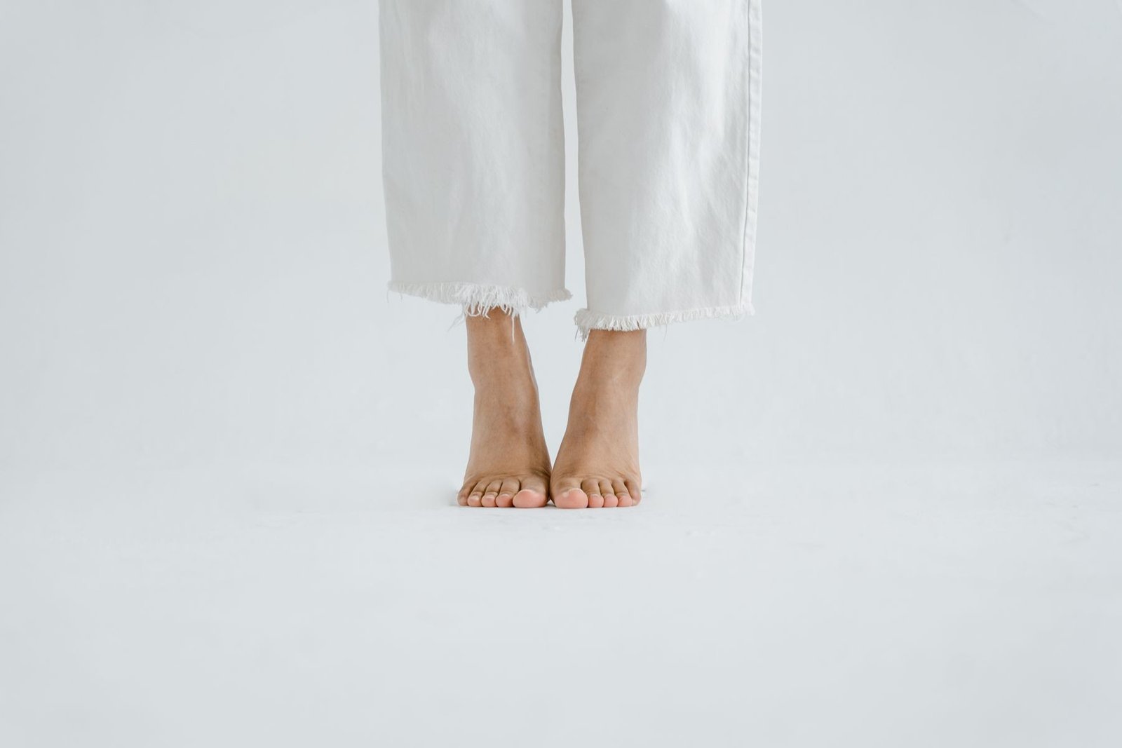 Bare feet in white trousers standing on a plain white floor
