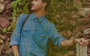 Man standing beside a stone wall and greenery