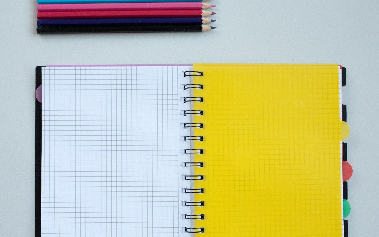 An open notebook and coloured pencils on a light surface