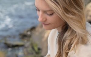 A blonde woman writing in a notebook outdoors beside water