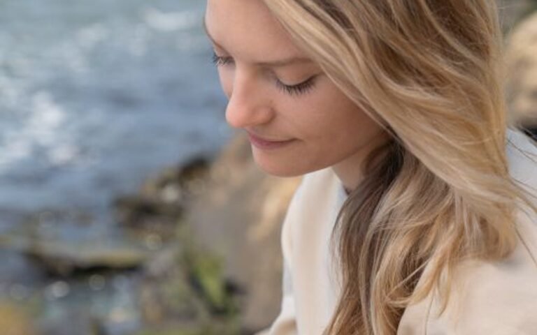 A blonde woman writing in a notebook outdoors beside water