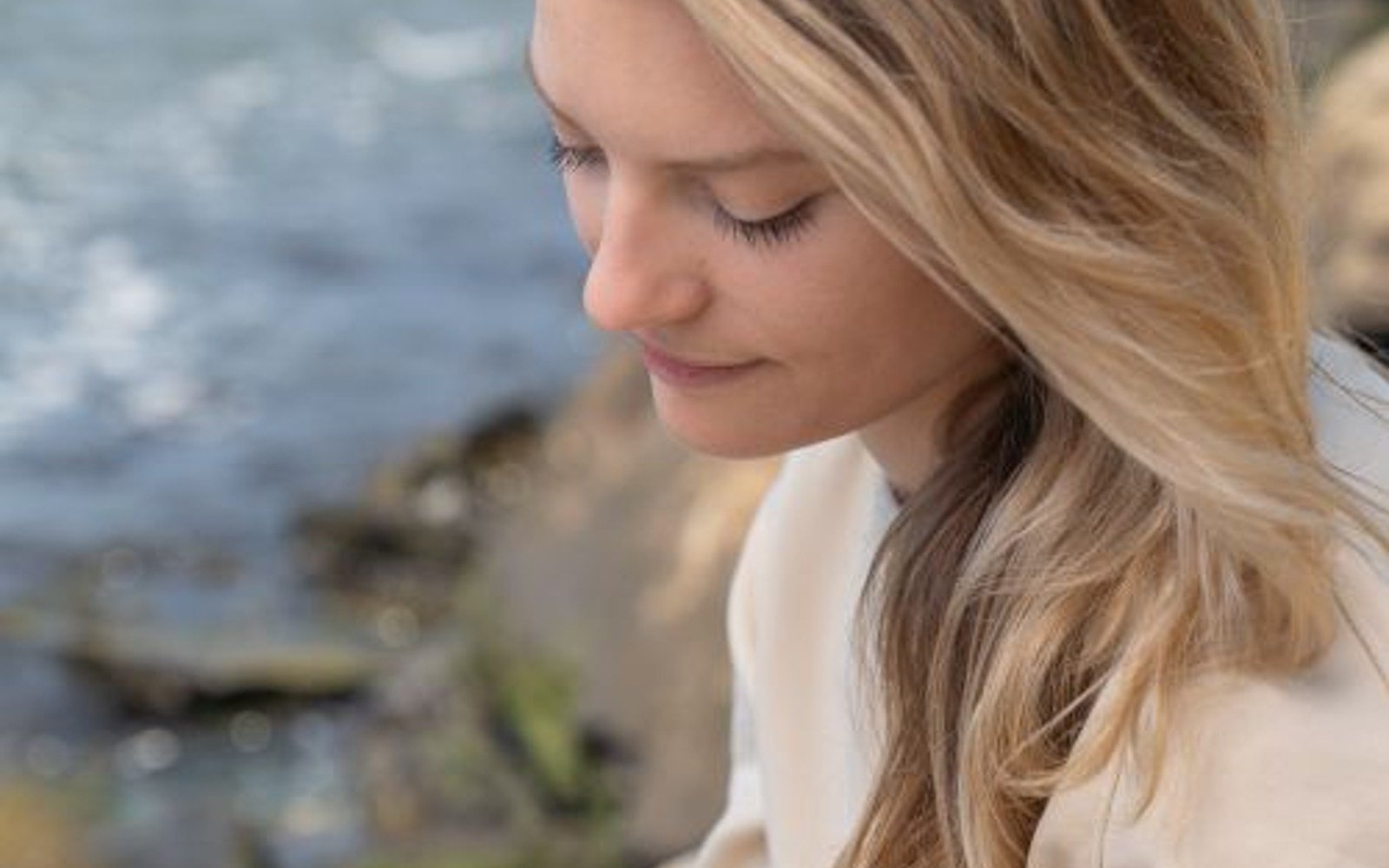 A blonde woman writing in a notebook outdoors beside water
