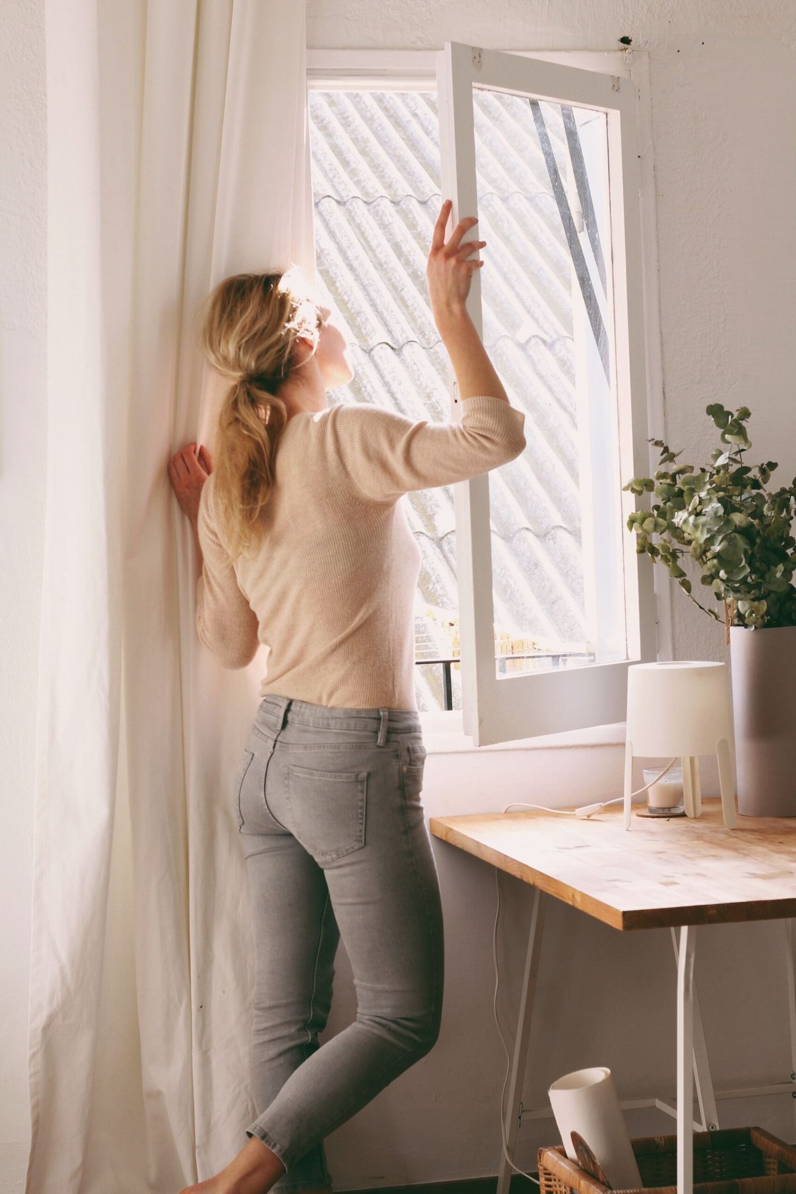 Woman looking out through an open window in a quiet daylight room