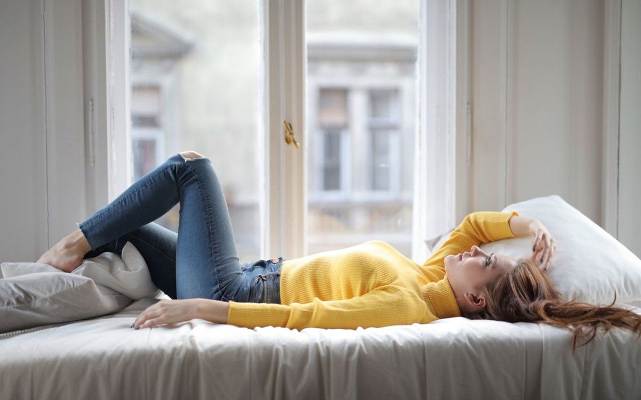 Woman resting on a bed near a bright window