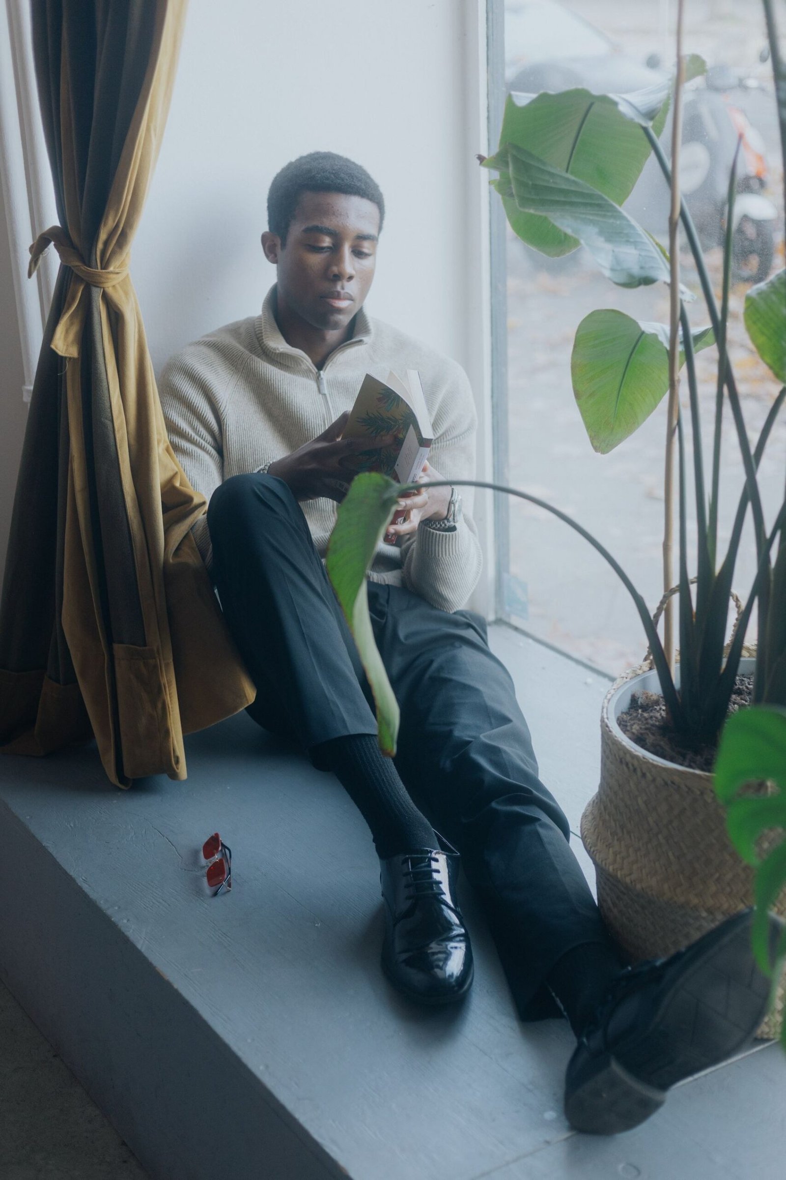 Man reading quietly by a window with a plant