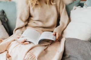 Person resting with a book and blanket on a sofa
