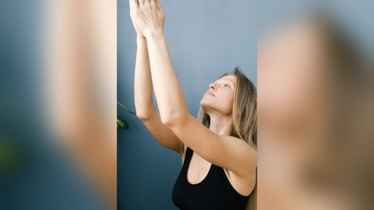 A blonde woman raising her arms in front of her while looking upwards in a room