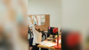 A woman stretching her arms above her head while seated at an office desk