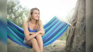 A young woman sitting in a striped hammock under a tree, smiling