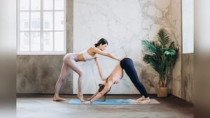 A yoga instructor guiding a student through a downward-facing dog pose in a bright studio