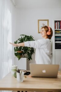 A woman stretching her arms at her desk with a laptop, a plant beside her