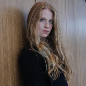 A young blonde woman leaning against wooden doors, pausing thoughtfully
