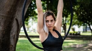 A woman with blonde hair holding an aerial exercise ring above her head in a park